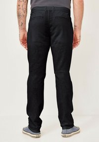 Black denim jeans with a straight-cut fit, featuring rear pockets and subtle texture. Paired with gray sneakers and a plain shirt.