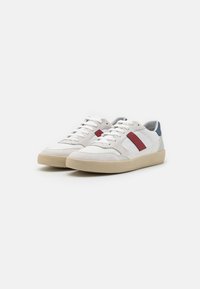 Sneaker bianchi e grigi con dettagli rossi e blu, dotati di una tomaia in pelle liscia e suede, lacci piatti e una suola in gomma testurizzata.