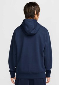 Felpa blu navy con cappuccio, polsini e orlo a costine. Tessuto morbido e texturizzato con una vestibilità rilassata, che mostra la vista da dietro dell'indossatore.
