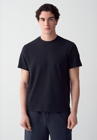 T-shirt nera a maniche corte con un design semplice e colletto rotondo. Realizzata in tessuto morbido, presenta una vestibilità comoda e senza motivi visibili.