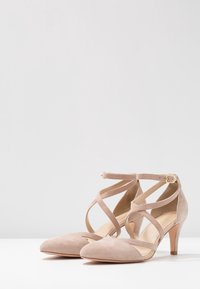 Scarpe con tacco alto in suede beige, dalla punta affusolata, con cinturini incrociati e una fibbia alla caviglia per la chiusura.