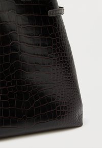 Μαύρη τσάντα χειρός από ψεύτικο δέρμα με υφή κροκόδειλου, κωνικό σχήμα και διακριτικό αντίθετο ράψιμο. Διαθέτει λεία, γυαλιστερή επιφάνεια.