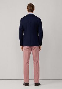 Blazer blu navy, vestibilità sartoriale, con taglio dritto; abbinato a pantaloni rosa chiaro. Tessuto morbido, design elegante e scarpe scure.