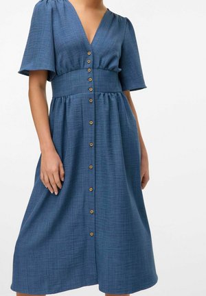 Frau trägt ein blaues Midikleid mit kurzen Ärmeln, V-Ausschnitt, tailliertem Schnitt und einer Reihe von Knöpfen vorne.