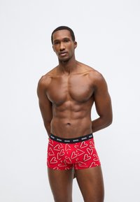 Piros boxermadaras alsónadrág szívmintával, fekete elasztikus derékpánttal, márkajelzéssel. Az anyag simának és testhezállónak tűnik.