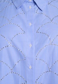 Light blue button-up shirt with vertical white stripes, featuring decorative silver stitching in a scalloped pattern.