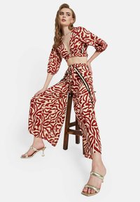 Top corto de estampado rojo y crema con mangas de tres cuartos y pantalones de pierna ancha a juego. Cuenta con una cintura ajustable con cordón y acentos laterales.