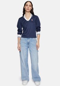 Polo a maniche lunghe blu navy con accentuazioni del colletto bianco e polsini a costine. Abbinato a jeans a gamba larga azzurri e sneakers bianche.