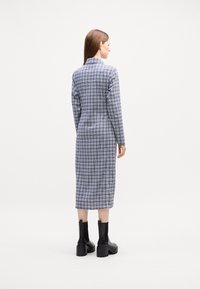 Abito camicia lungo a plaid blu e bianco con colletto, maniche lunghe, chiusura a bottoni e linea dritta, abbinato a stivali neri alla caviglia.
