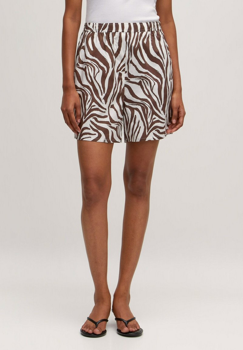 Bruine en witte zebra-print shorts met een elastische tailleband, lichte stof en een relaxte pasvorm. Gestyled met simpele zwarte sandalen.