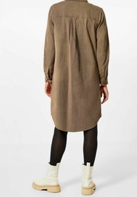 Abito lungo marrone a maniche lunghe con pieghe sul retro, orlo arrotondato e polsini con bottoni, abbinato a collant neri e stivali alla caviglia in crema con platform.