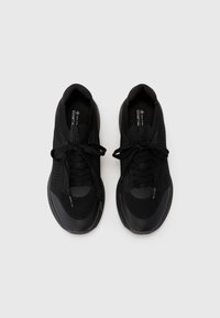 Chaussures de sport noires avec une tige en maille et une semelle en caoutchouc solide. Les caractéristiques incluent des lacets ronds, des accents texturés et un design épuré.