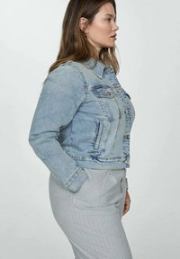 Lyseblå denimjakke med klassisk snit, knaplukning fortil, to brystlommer og en let slidtegn detail. Glat tekstur.