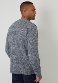 Maglione grigio lavorato a maglia con un motivo testurizzato e macchiato, scollo a girocollo e polsini a costine, abbinato a jeans blu scuro.