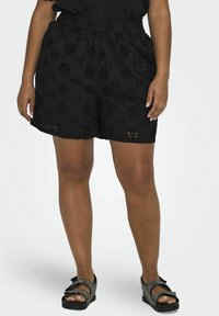 Crne kratke hlače s cvjetnim vezom i elastičnim pojasom. Lagani materijal s izrezbarenim uzorcima, uparen s crnim sandalama s ukrasima.