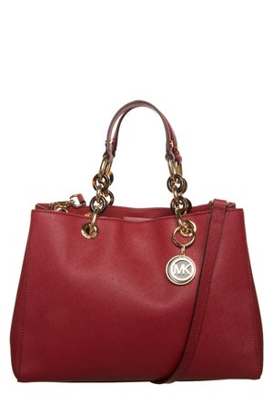 Sac à main en cuir rouge avec poignées chaîne dorées et un charm logo MK, avec une bandoulière amovible.