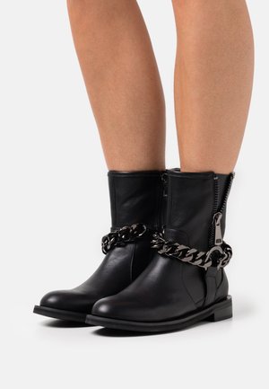 Bottines noires en cuir avec une finition texturée, dotées d'une fermeture éclair latérale et d'un accent de chaîne métallique épaisse. Bout carré et petit talon.