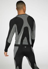 Langärmliges Sportshirt und Leggings in Schwarz mit weißen geometrischen Mustern, ausgestattet mit einem dehnbaren, figurbetonten Design und texturalen Kontrasten.