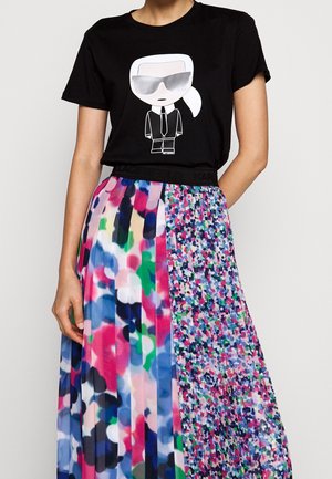 T-shirt noir avec un graphisme représentant un personnage portant des lunettes de soleil, associé à une jupe plissée multicolore avec des motifs abstraits.