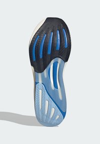 Suela de una zapatilla que presenta un diseño de banda de rodadura de goma negra y azul, con una capa texturizada de azul claro y acentos crema, destacando surcos profundos.