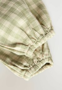 Tissu à carreaux verts clairs avec des poignets élastiques. Texture douce, présentant des carreaux foncés et clairs alternés dans un motif tissé.