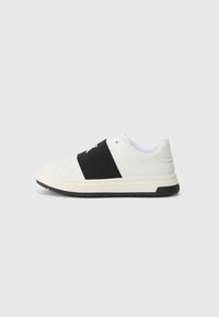 Hvite sneakers med et svart elastisk bånd over midtfoten, textured skinnøvre, og en gummisåle med et svakt mønster.