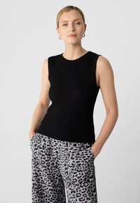 Top in maglia nera aCostine con scollatura rotonda, abbinato a pantaloni grigi con stampa leopardata e tasche laterali. Aggiornamento su abbigliamento casual.