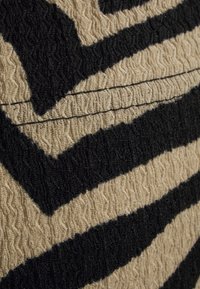 Tessuto testurizzato con audaci strisce zebra nere e beige. Il materiale è elastico con una superficie ondulata, che mette in risalto il motivo e il contrasto di colori.