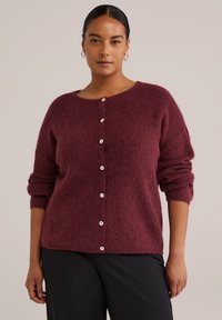 Burgundy stickad cardigan med lös passform, rund halsringning och vita knäppningar fram. Mjuk textur och upprullade ärmar.