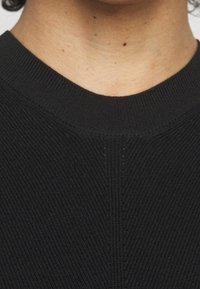 Czarny prążkowany kołnierz ze swetra o gładkiej fakturze. Projekt zawiera subtelne ukośne linie i dopasowany dekolt.