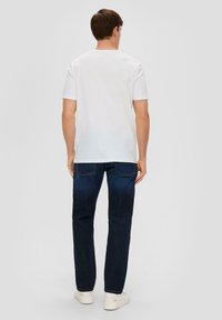Weißes T-Shirt mit kurzen Ärmeln, kombiniert mit dunkelblauen Jeans. Die Jeans haben einen geraden Schnitt und werden durch weiße Sneakers ergänzt.