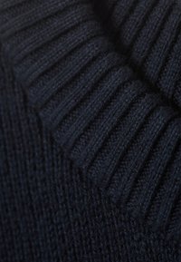 Närbild av tjockt, mörkblått stickat tyg med växlande vertikala ribb- och texturmönster.