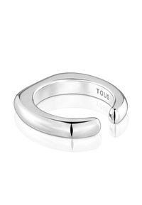 Anello aperto in argento lucido con bordi arrotondati e inciso "TOUS" all'interno della fascia, poggiato su una superficie bianca riflettente.