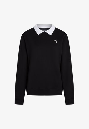 Μαύρο πουλόβερ με μακριά μανίκια, λευκό γιακά και μικρό λογότυπο με πρόσωπο που φοράει γυαλιά ηλίου στο πάνω αριστερό μέρος του στήθους.