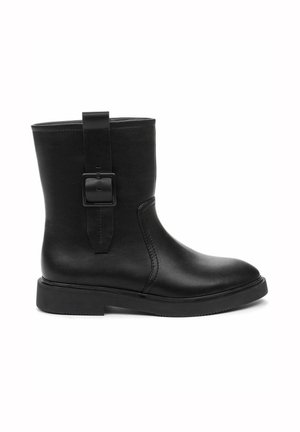 Botte en cuir noire montant jusqu'au milieu du mollet, avec bout arrondi, semelle plate et sangle décorative avec boucle carrée sur le côté extérieur.