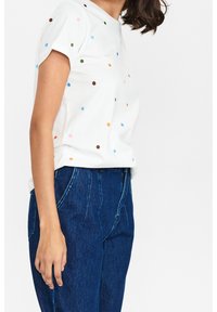 Witte T-shirt met korte mouwen en meerkleurige stippenpatronen, gecombineerd met hoog-waisted donkerblauwe spijkerbroek. Zachte katoenen textuur, ontspannen pasvorm.