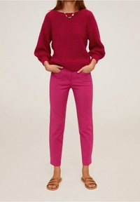 Magenta knitted sweater with balloon sleeves, paired with fitted pink trousers and brown sandals, showcasing a glossy necklace as an accent.