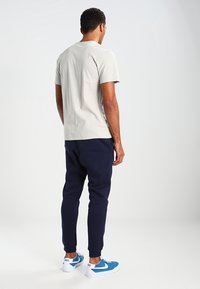 Una camiseta gris clara combinada con pantalones jogger azul marino. Los joggers tienen un diseño ajustado, y el conjunto se complementa con zapatillas en azul y blanco.