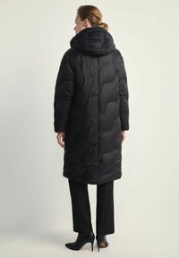 Czarna kurtka puchowa z kapturem, z pikowanym wzorem i lekko wydłużonym krojem, w połączeniu z czarnymi spodniami i szpilkami.
