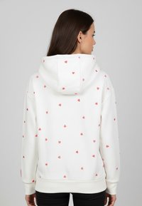 White hoodie featuring small pink heart patterns, a front pocket, and a drawstring hood; made from a soft, textured material.