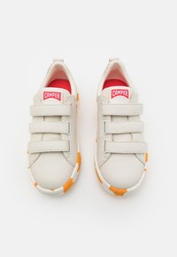 Scarpe in pelle bianca con tre fascette in velcro grigie, accenti in gomma arancione e bianca sulla suola, rivestimento interno rosso e logo CAMPER sulla linguetta.