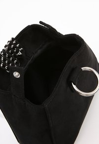 Svart mocka handväska med en strukturerad form, med en silverring som accent och en vävd detalj på stängningen. Insidan är fodrad med tyg.