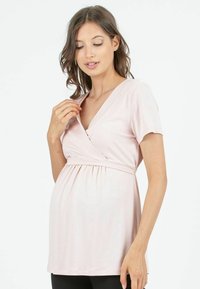 Różowa bluzka ciążowa wykonana z miękkiego materiału, z dekoltem w kształcie V, krótkimi rękawami i marszczonym w pasie, zapewniająca komfort w czasie ciąży.