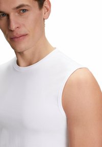 White sleeveless top made of smooth, lightweight fabric. Features a round neckline and fitted design, showcasing the shoulder and upper arm.