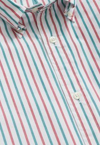 Kariertes Hemd aus weißem Stoff mit roten und türkisfarbenen vertikalen Streifen. Verfügt über Knöpfe und kontrastierende Nähte entlang der Knopfleiste.