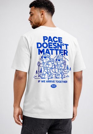 Man wearing white T-shirt with blue design showing two hiking cats and text saying "Pace doesn't matter if we arrive together."