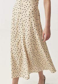 Crème midi-jurk met zwarte stippen, zachte stof, A-lijn vorm en een licht uitlopende zoom. Zijkant naden zijn zichtbaar.