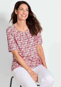 Korte mouwen roze top met een bloemenpatroon met rode en witte bloemen. Ronde halslijn en zachte stof, gecombineerd met witte broek.