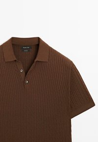 Brun stickad polo med kort ärm, med ett ribbat mönster, två knappar framtill och en klassisk krage.