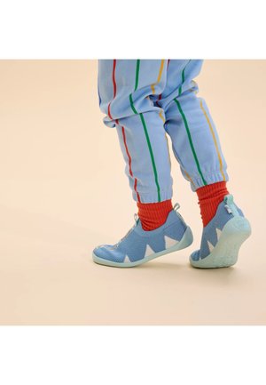 Lichtblauwe mesh schoenen met witte driehoekige accenten, flexibele zool en trekband; gecombineerd met rode geribde sokken en lichtblauwe gestreepte broeken.